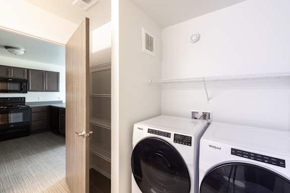 A white wall with a washing machine and dryer in front of it.