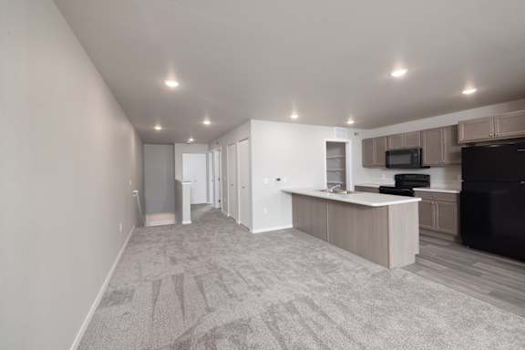 A spacious living room with a grey carpet and a kitchen area with a microwave and oven.