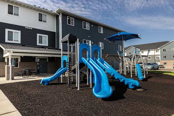 A playground with a blue slide in front of a building.