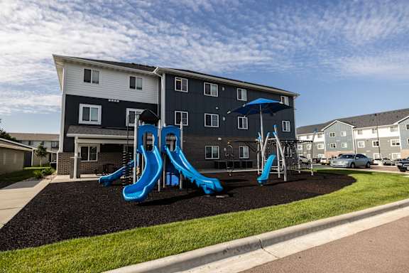 A playground with a blue slide in front of a two-story building.