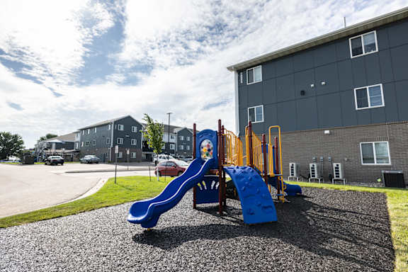 A playground with a blue slide in front of a grey building.