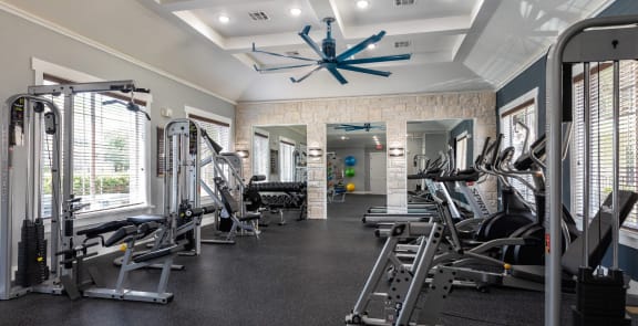a large fitness room with cardio equipment and windows