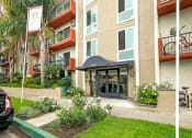 Thumbnail 41 of 41 - Mar Vista CA Apartments for Rent - Vista - Property Exterior with Tan Walls, White Trim, Orange Balconies, and Landscaped Plants Around the Front
