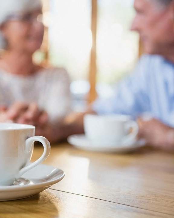 an older couple sitting at a table with cups of coffee
