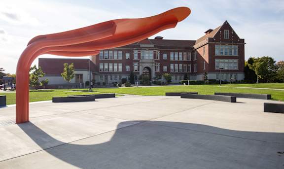 A large orange sculpture in the foreground with a building in the background.