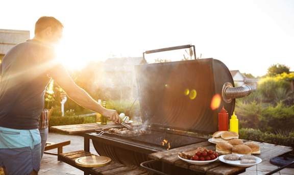 A man grilling food on a barbecue in the sunset.