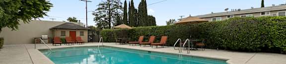 Studio Apartments in Van Nuys CA - Colonial Manor - Aqua Pool with Surrounding Hedge, Poolside Seating, and Umbrellas
