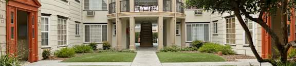 Pet Friendly apartments in Van Nuys CA - Colonial Manor - Outdoor Courtyard with Tan Building Exterior, Green Landscaping, Paths, Stairwell, and Trees