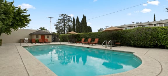 Studio Apartments in Van Nuys CA - Colonial Manor - Aqua Pool with Surrounding Hedge, Poolside Seating, and Umbrellas