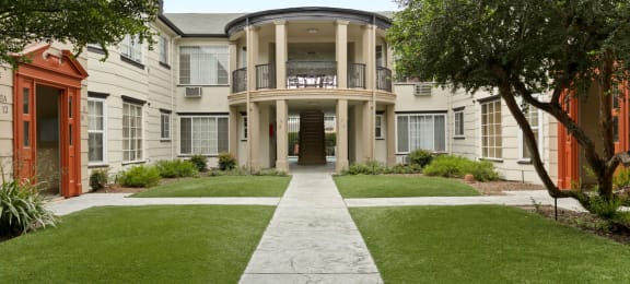 Pet Friendly apartments in Van Nuys CA - Colonial Manor - Outdoor Courtyard with Tan Building Exterior, Green Landscaping, Paths, Stairwell, and Trees