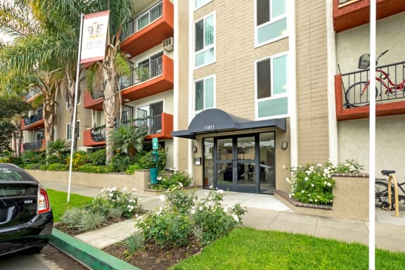 Mar Vista CA Apartments for Rent - Vista - Property Exterior with Tan Walls, White Trim, Orange Balconies, and Landscaped Plants Around the Front