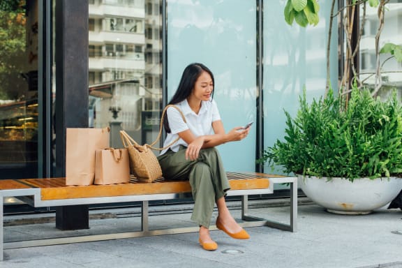 young woman sitting on a bench with shopping bags and looking at her phone