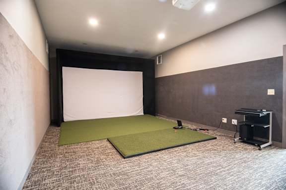 A room with a projector screen, green mats, and a black cart.