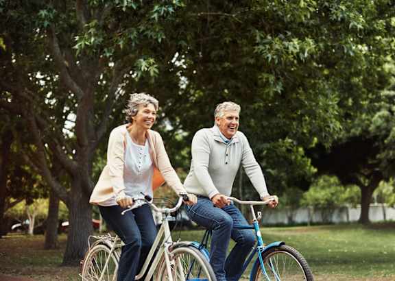 An older couple riding a bicycle together in a park.