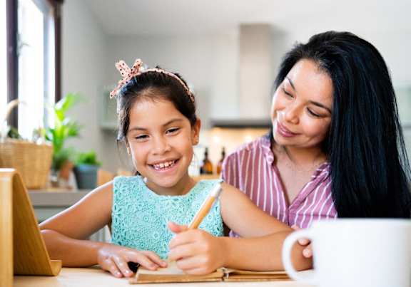 a woman and a girl sitting at a table using a laptop