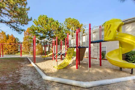 Playground jungle gym and playground slides in a bed of mulch with trees, and swings in the background