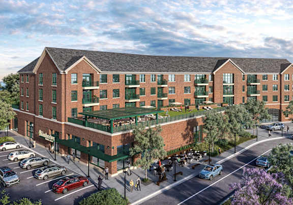 A large red brick building with a green awning and a parking lot in front.
