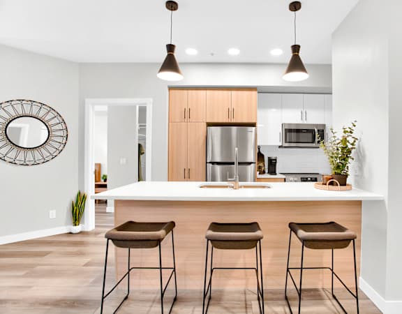 A modern kitchen with a white island and brown bar stools.