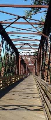 A bridge with a metal truss design and a wooden walkway.