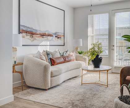 A living room with a beige couch, a plant, and a painting on the wall.