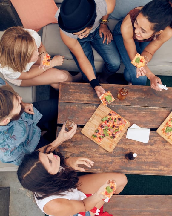group of five friends eating pizza