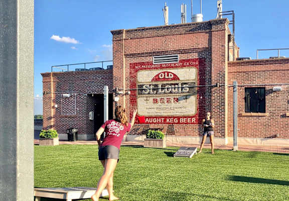 A woman is playing frisbee in front of a building with a sign that reads "Old St. Louis Beer".