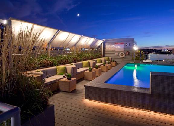 A rooftop pool area with a hot tub and seating area.