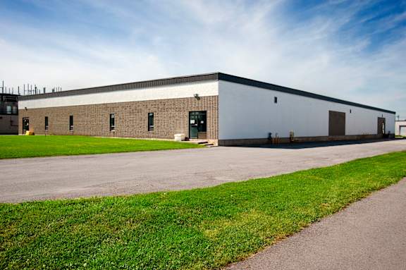A large industrial building with a grey roof and a green lawn in front.
