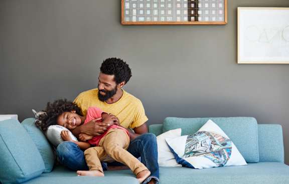 A man and a child are sitting on a blue couch.