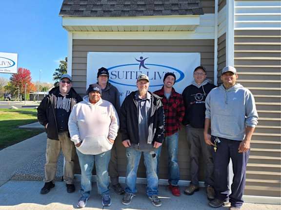 A group of people are standing in front of a Suite Living building.