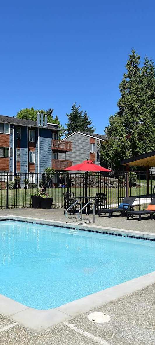 A swimming pool surrounded by a black fence with red umbrellas and chairs.