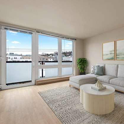 A living room with a grey couch, a coffee table, and a large window overlooking a cityscape.
