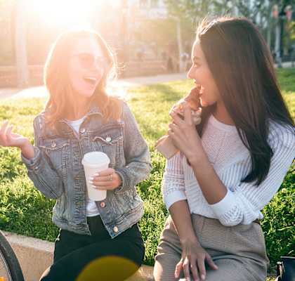 two women sitting in a park talking on their cell phones