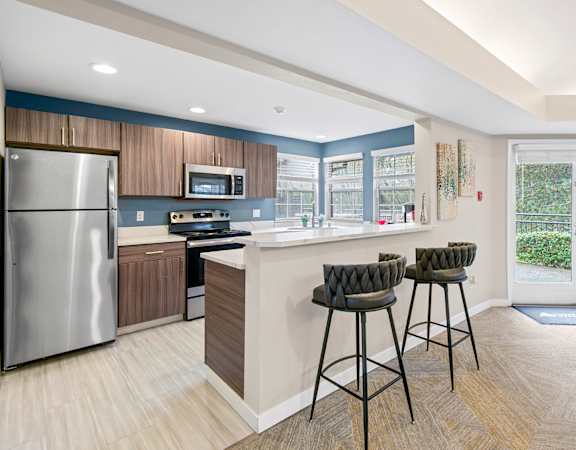 A kitchen with a refrigerator, stove, and bar stools.