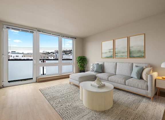 A living room with a grey couch, a coffee table, and a large window overlooking a cityscape.