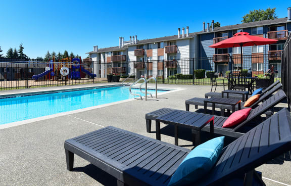A pool area with black lounge chairs and a red umbrella. at Brookstone, Washington, 98198
