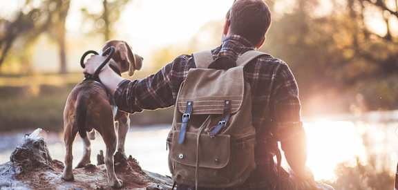 A man with a backpack is sitting on a rock with his dog.