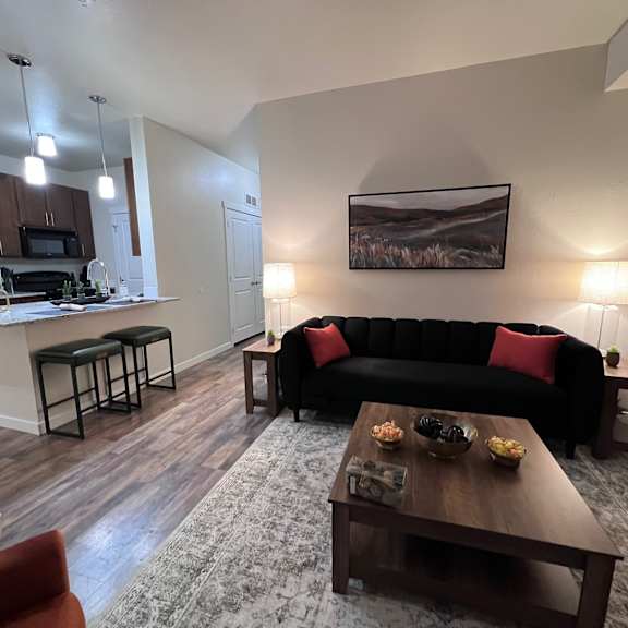 A living room with a black couch and a painting on the wall.