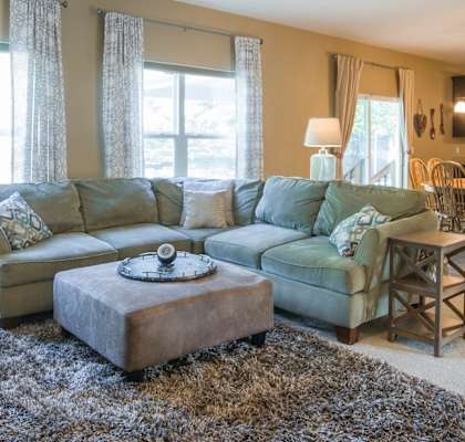 A living room with a brown chair, a brown ottoman, a green couch, and a brown rug.