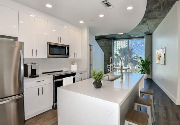 a kitchen with white cabinetry and a large white island with a sink and two stools at Element, Florida, 33602