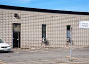 Thumbnail 3 of 6 - A white car is parked in front of a building with a sign that says Dynamic Precision.
