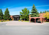 Thumbnail 1 of 3 - A parking lot with a building and trees in the background.