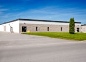 Thumbnail 1 of 4 - A large industrial building with a parking lot in front.