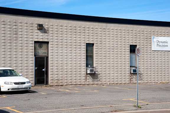 A white car is parked in front of a building with a sign that says Dynamic Precision.