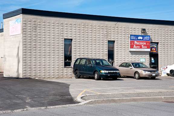 Two cars are parked in front of a building with a sign that says Precision Auto Tech.