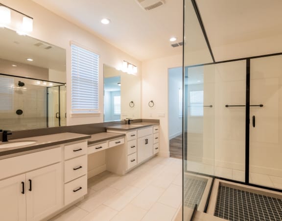 A modern bathroom with a walk-in shower and double sinks.at Crocker Village – Single Family Homes, Sacramento