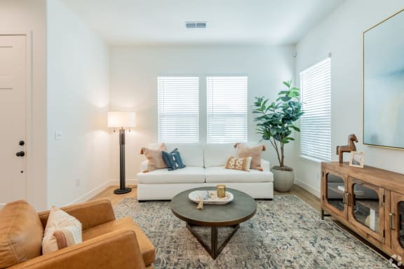 A living room with a white couch, a brown leather chair, a coffee table, and a plant.at Crocker Village – Single Family Homes, Sacramento, 95818