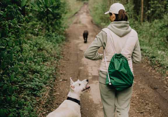 A woman walking a dog on a dirt road.
