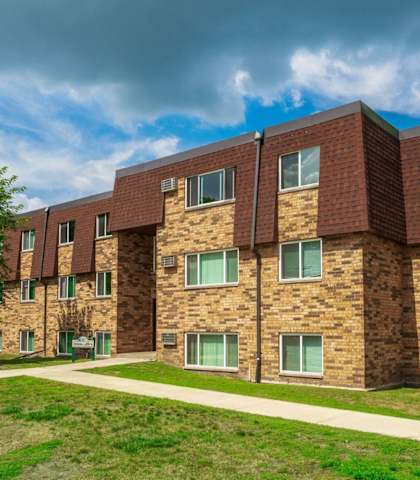 a brick apartment building with green grass and a sidewalk