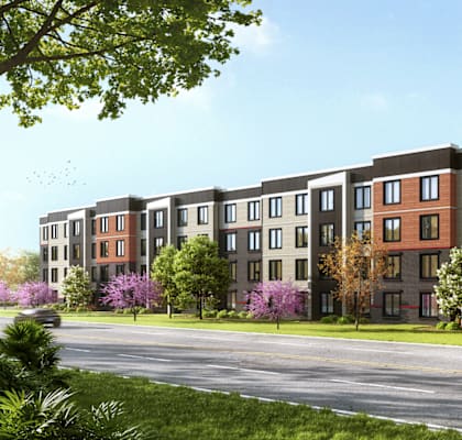 A row of modern apartment buildings with trees and a car driving by.